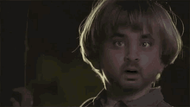 a man with blonde hair and a beard is holding a knife and making a surprised face .