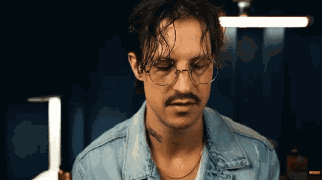 a man wearing glasses and a denim jacket has a tattoo on his chest