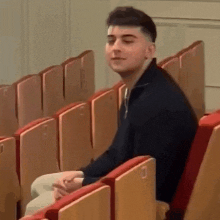 a man is sitting in a row of wooden seats in a theater .