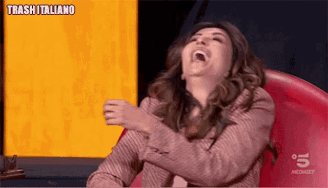 a woman is laughing while sitting in a red chair on tv .
