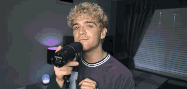 a man in a purple shirt is holding a sony microphone