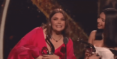 a woman in a red dress is holding a trophy on a stage while another woman laughs .