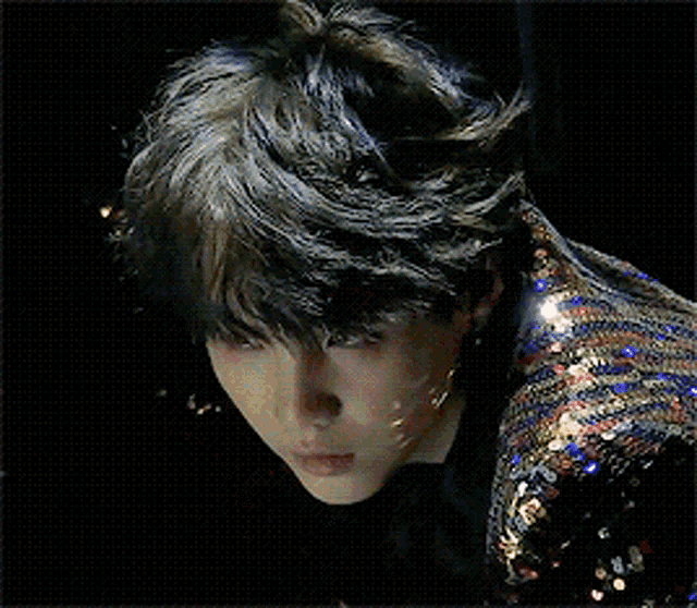 a close up of a person 's face with a black background and a sequined jacket .