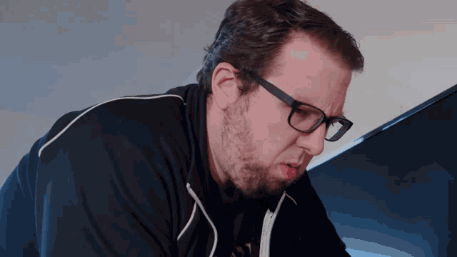a man wearing glasses and a black jacket looks down at something