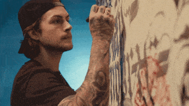 a man with tattoos on his arm is writing on a wall with a marker
