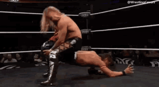 two men are wrestling in a wrestling ring with a referee in the background .