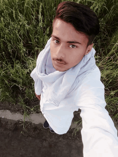 a young man wearing a white shirt and a scarf stands in front of tall grass