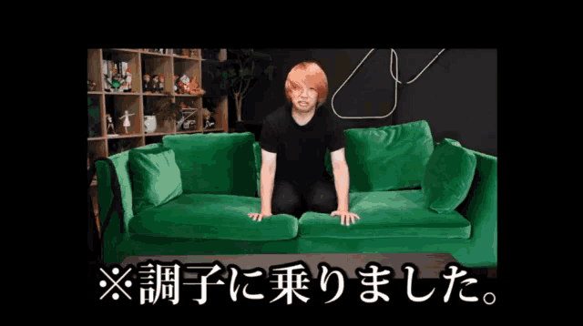 a man with red hair is sitting on a green couch in a black room
