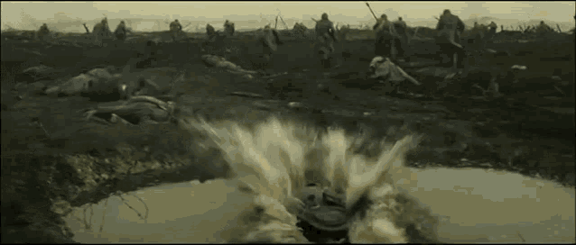 a group of soldiers are running through a muddy field with a tank exploding in the middle of the field .