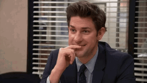 a man in a suit and tie is sitting in front of a window with his hand on his chin .