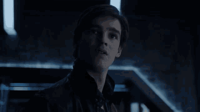 a man in a black jacket is standing in a dark room with stairs .