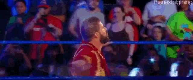 a man in a red shirt is standing in a wrestling ring in front of a crowd of people .