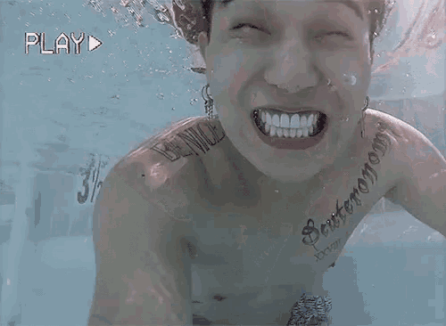 a man with a tattoo on his neck is swimming underwater and the play button is visible in the background