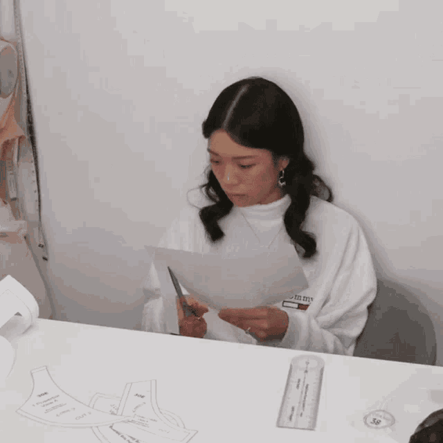 a woman in a tommy hilfiger sweatshirt is cutting a piece of paper