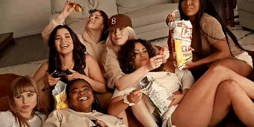 a group of women are laying on a couch and one of them is holding a bag of lays potato chips