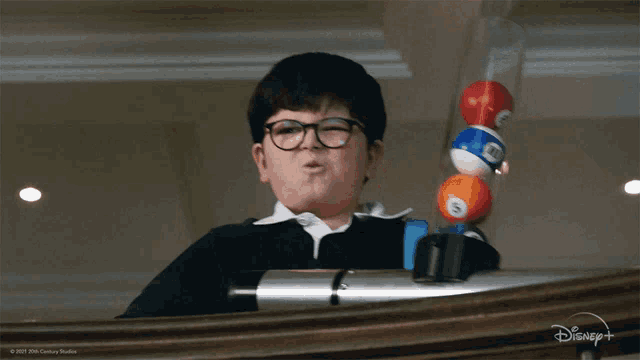 a boy with glasses is holding pool balls in front of a disney + logo