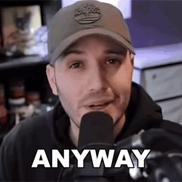 a man wearing a hat is talking into a microphone with the word anyway written on the bottom of his face .