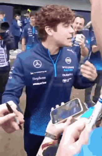 a man wearing a williams racing jacket is being interviewed