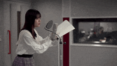 a woman is singing into a microphone while holding a piece of paper
