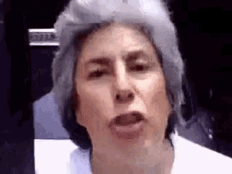 a woman with gray hair is making a funny face while wearing a white shirt .