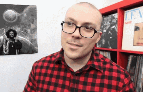 a man wearing glasses and a red and black plaid shirt is standing in front of a dare album