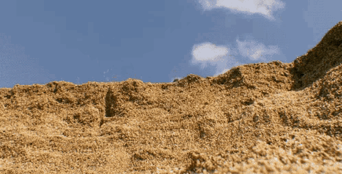 a large pile of dirt against a blue sky with clouds