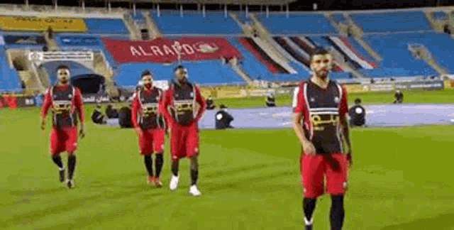 a group of soccer players are walking on a field in front of a stadium .