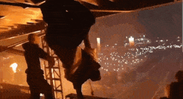 a man is hanging from the ceiling of a building while a fireworks display is going on in the background .