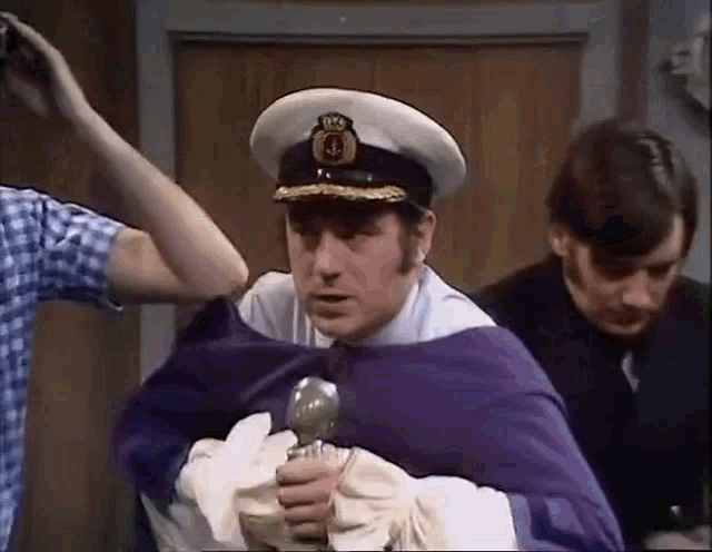a man in a captain 's hat is holding a sword while being held by two other men .
