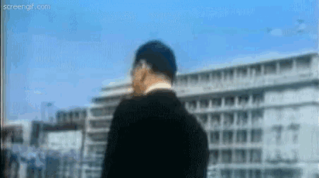 a man in a black suit is standing in front of a building .