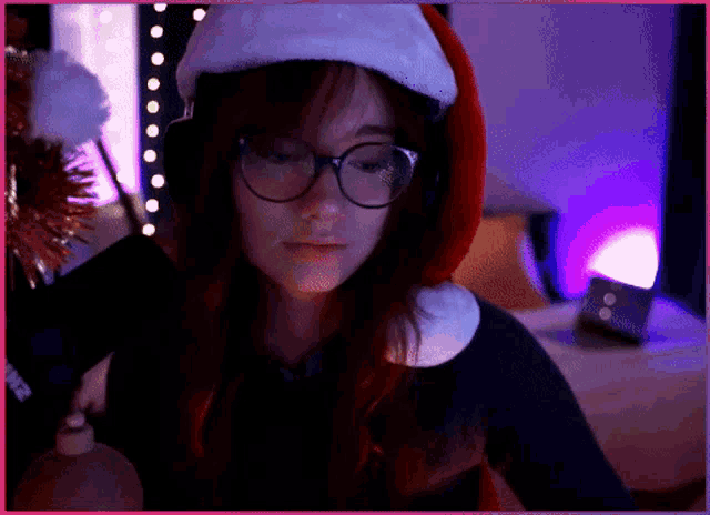 a woman wearing glasses and a santa hat looks down at something