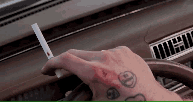 a man with a tattoo on his wrist holds a cigarette in his hand