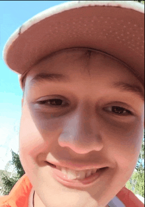 a young boy wearing a pink hat and an orange jacket smiles for the camera