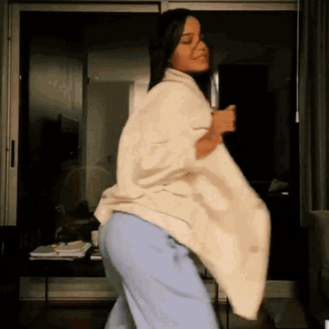 a woman in a white sweater and blue sweatpants is dancing in front of a sliding glass door