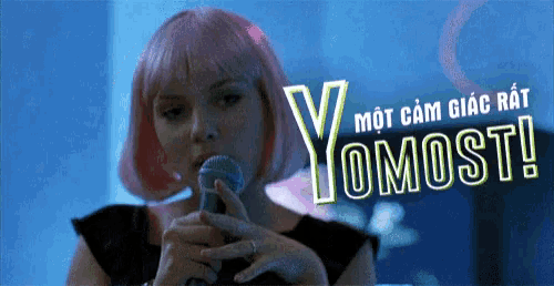a woman with pink hair is singing into a microphone and the words yomost are behind her