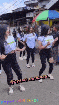 a group of women are dancing on a street with the words goyang muuuass on the bottom