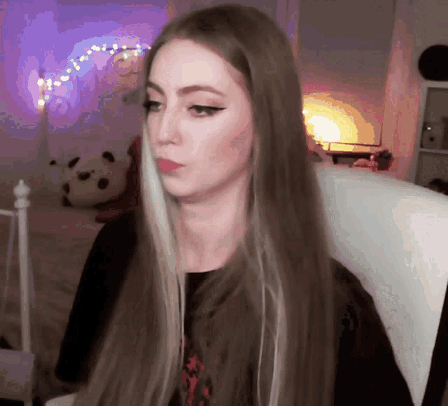 a woman with long hair is sitting in a chair in front of a bed