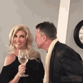 a man whispers into a woman 's ear while she holds a wine glass .