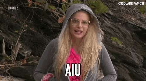 a woman wearing glasses and a hooded jacket says aiu in a pink shirt .