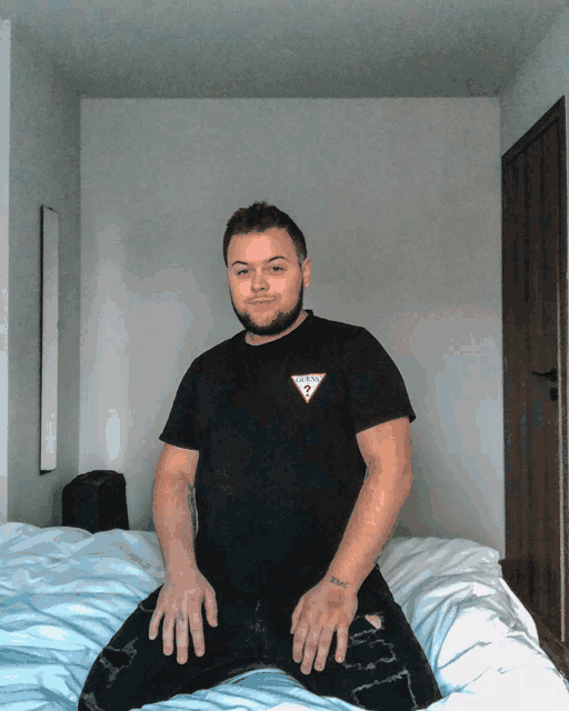 a man sitting on a bed wearing a black guess shirt