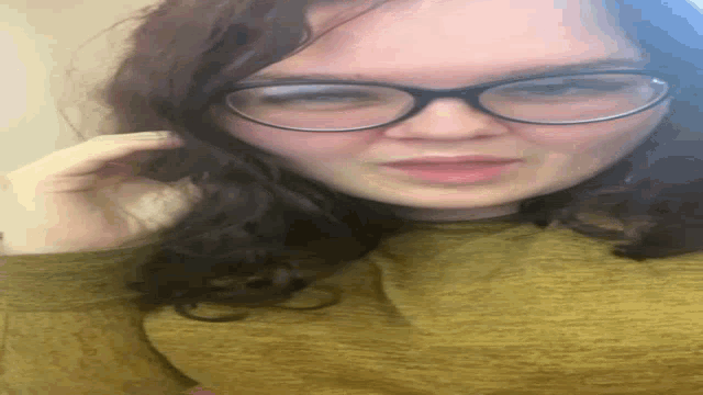 a woman wearing glasses and a yellow sweater is laying on her back .