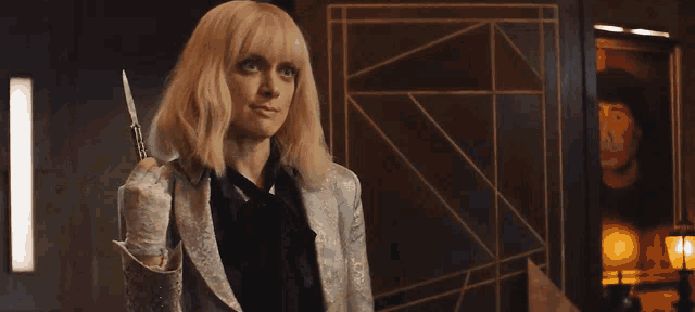 a woman with blonde hair is standing in a room with a painting on the wall behind her .