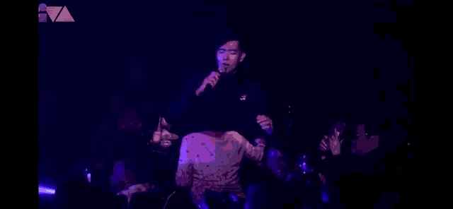 a man singing into a microphone in front of a crowd in a dark room