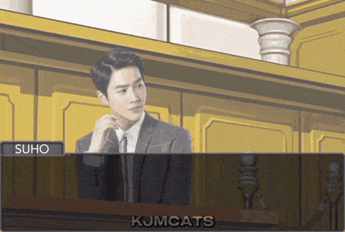 a man in a suit and tie sits in front of a microphone with the name suho visible