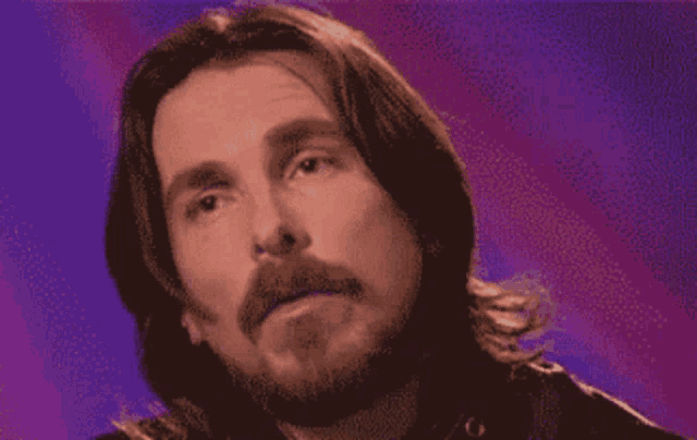 a man with long hair and a beard has a purple background