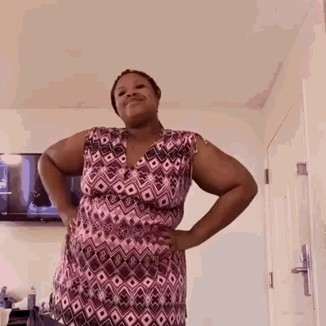 a woman in a pink dress is standing with her hands on her hips in a room .
