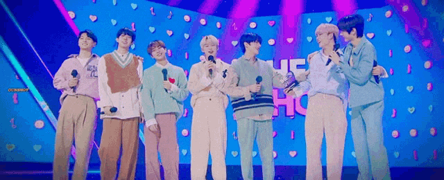 a group of young men are standing on a stage holding microphones and hugging each other .
