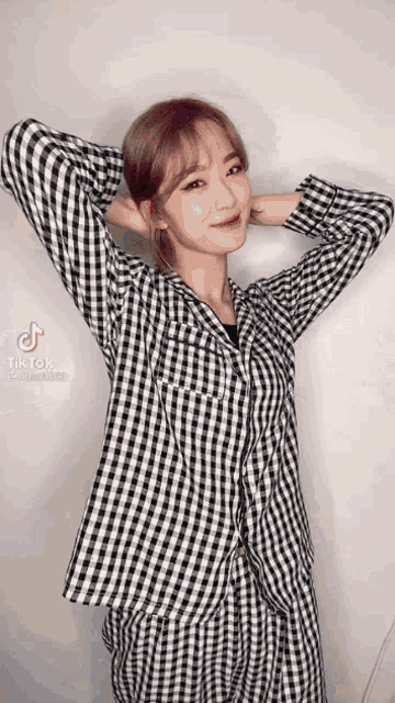 a woman in a plaid shirt is standing with her hands behind her head and smiling .