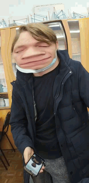 a man wearing a mask is holding a cell phone and making a funny face