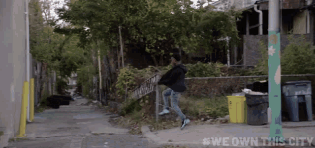 a man jumping over a fence with #we own this city written on the sidewalk